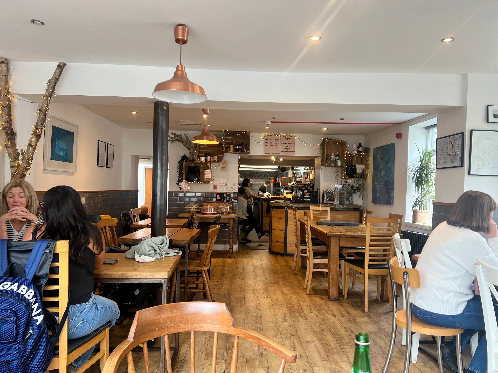 The Green's interior with wooden tables and chairs, customers seated beside the windows and the open kitchen at the back